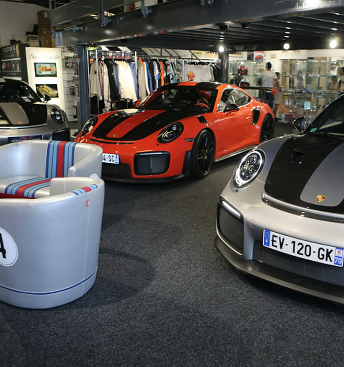 Le showroom : Porsche 911 GT2 RS orange et grise exposées parmi les vitrines de miniatures